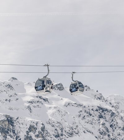 Zwei Gondeln der Schafbergbahn in Gargellen schweben vor einer beeindruckenden, schneebedeckten Bergkulisse. Die modernen Kabinen der Gargellner Bergbahnen heben sich klar vom hellen Winterhimmel ab, während im Hintergrund die majestätischen Gipfel der Montafoner Alpen aufragen. | © Gargellner Bergbahnen GmbH & Co KG, Daniel Zangerl