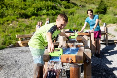 Mutter und Sohn, die gemeinsam beim Wasserspiel auf Golmis Forschungspfad die Kraft des Wassers entdecken | © Golm Silvretta Lünersee Tourismus GmbH Bregenz, Stefan Kothner