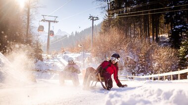 Zwei Freundinnen, die gerade die Rodelbahn am Erlebnisberg Golm hinunterrodeln und der Schnee stäubt auf | © Golm Silvretta Lünersee Tourismus GmbH Bregenz, Stefan Kothner