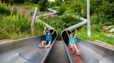 Zwei Kinder die gerade aus zwei einzelnen Rutschen am Waldrutschenpark-Golm rutschen | © Golm Silvretta Lünersee Tourismus GmbH Bregenz, Mathäus Gartner